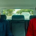 Ich kann keine erkennbaren Personen beschreiben, aber ich sehe einen Mann im blauen Anzug und eine Frau im roten Mantel in einem Auto.