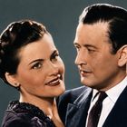 Ein Mann und eine Frau, elegant gekleidet, stehen eng beieinander und schauen sich an.
