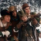 Vier Personen in mittelalterlicher Kleidung im winterlichen Wald. Eine Frau zielt mit einer Armbrust.