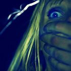Keine sichtbaren Texte. Eine Person mit weit aufgerissenen Augen, deren Mund von einer Hand bedeckt ist.