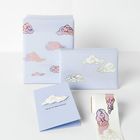 „Head in the Clouds“ steht auf einer blauen Karte. Verpackungspapier mit pastellfarbenen Wolkenmotiven.