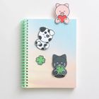 Keine Texte erkennbar. Ein Notizbuch mit bunten Aufklebern: Schwein, Hund, Katze, alle mit Kleeblättern.