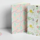 Zwei Notizbücher mit floralen Mustern. Links ein pastellfarbenes Muster, rechts ein bunteres Design. Schreibutensilien liegen daneben.