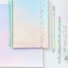 Notizbücher mit bunten Spiralbindungen, zwei Bleistifte, dekoratives Klebeband und kleine Einhorn-Radiergummis in Pastellfarben.