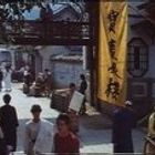 Ein gelbes Banner mit asiatischen Schriftzeichen hängt an einem Gebäude in einer geschäftigen Straßenszene mit Menschen.