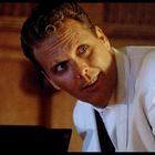 Ein Mann in einem weißen Kittel blickt freundlich nach oben. Der Hintergrund ist unscharf und warm beleuchtet.