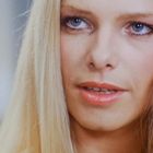 Es gibt keinen Text zu erwähnen. Eine Frau mit langen blonden Haaren und blauen Augen blickt leicht lächelnd.