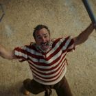 Ein Mann in einem gestreiften Pullover schaut nach oben und hält einen großen Metalldraht und eine Stange in der Hand.