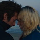 Ein Mann und eine Frau neigen ihre Köpfe zueinander am Strand bei Abenddämmerung.