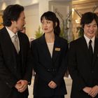 Drei Personen in eleganter Kleidung, zwei Männer und eine Frau, stehen nebeneinander. Alle tragen Namensschilder.