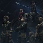 Eine Gruppe von Menschen in futuristischen Outfits. Ein Schädel-Logo ist sichtbar. Ihre Haltung wirkt entschlossen.