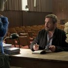 Ein Mann sitzt an einem Tisch und signiert ein Buch. Eine Frau steht davor. Im Raum sind viele leere Stühle.