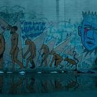 Graffiti-Wand mit: "FUN LACK HUMAN EVOLUTION", "IN THE LAND OF THE BLIND", "NOTHING IS REAL". Evolution und Gesichter illustriert.