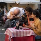 Der Text "Casetta di Trastevere" ist auf einer Markise. Vier Personen sitzen an einem Tisch mit rot-weiß kariertem Tuch.
