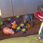 Verschiedene Spielzeuge stehen auf dem Boden, darunter ein Dino, ein Schwein und eine Person mit rotem Hut.