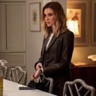 Eine Frau steht in einer modernen Küche, trägt eine dunkle Jacke und schaut nachdenklich. Im Hintergrund sind Bilder von Vögeln.