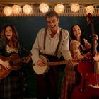 Eine Frau mit Gitarre, ein Mann mit Banjo und eine Frau mit Kontrabass unter Lampions, alle lächelnd.