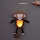 Eine Laterne in Form eines Affen, der von einer Hand an einem Stab gehalten wird. Die Lampe leuchtet warm im Bauch.