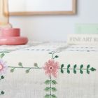 Der Text "FINE ART R..." ist auf dem Rücken eines Buches zu sehen. Ein Tischläufer mit rosafarbenen, gestickten Blumen darauf.