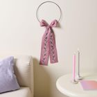 Text fehlt. Ein schwarzer Ring mit rosa Schleife und Blumenmuster hängt an der Wand. Daneben brennen rosa und lila Kerzen.