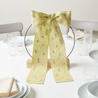 Gelbe Stoffschleife mit Blumenmuster, auf einem Tisch dekoriert mit Gläsern, weißen Tellern und Stoffservietten.