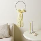 Ein Metallring mit gelber Schleife hängt an einer Wand, daneben Sofa und Tisch mit gezwirbelten Kerzen und einer kleinen Tasse.