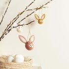 Drei Filz-Hasenköpfe hängen an Zweigen, darunter ein Korb mit weißen Eiern.