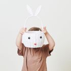 Ein Kind hält einen weißen Korb mit Hasengesicht und Ohren vor dem Gesicht. Das Kind trägt ein braunes T-Shirt.