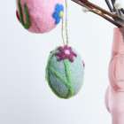 Filzkugeln mit Blumenmuster hängen an Zweigen in einer rosa Vase.