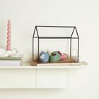 Keine Texte vorhanden. Eine dekorative Szene mit einer rosa Kerze, einem Bücherstapel und farbigen Filzeiern in einem kleinen Gestell.