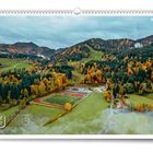 „9“, „11FREUNDE“. Herbstliche Landschaft mit Sportplatz, umgeben von bunten Wäldern und Hügeln.