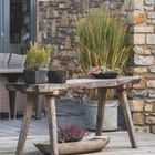 Oktober 2027 Kalenderblatt. Ein rustikaler Tisch mit Pflanzen vor einer Steinmauer und Fenstern im Außenbereich.