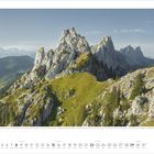 Text: "Die markante Kalksteinformation 'Gastlosen' in den Freiburger Voralpen wird 'Schweizer Dolomiten' genannt."

Majestätische graue Kalksteinklippen und sanfte grüne Hügel mit vereinzelten Bäumen.