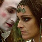 Zwei Personen in historischer Kleidung stehen sich nah gegenüber. Eine Person trägt eine verzierte Kopfbedeckung.