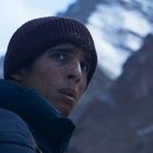 Ein Mann in warmer Kleidung blickt besorgt nach rechts, Berglandschaft im Hintergrund.
