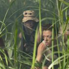 Mehrere Menschen kriechen durch dichtes, hohes Gras. Sie wirken konzentriert und angespannt.