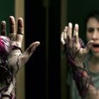 Eine Person schaut erschrocken in einen Spiegel. Ihr Arm hat ein filigranes, organisches Muster mit einem leuchtenden Punkt.