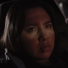 Eine Frau sitzt in einem dunklen Auto und sieht ernst aus. Ihr Gesicht wird von sanftem Licht beleuchtet.