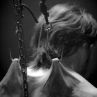 Ein Rücken mit zwei Haken, die in die Haut eingehakt sind, von Ketten aufgehängt, in Schwarz-Weiß gehalten.