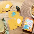 "Krake im Stall" Kartenspiel auf Holztisch, bunte Karten mit einer blauen Krake, dazu Schale mit Snacks und Getränk.