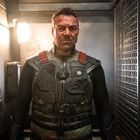 Ein Mann in Kampfausrüstung steht in einem engen, düsteren Raum. Sein Gesicht ist schmutzig und entschlossen.