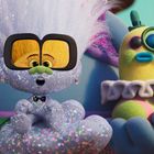 Eine glitzernde Figur mit großer Brille hält ein buntes, flauschiges Wesen mit Monokel.