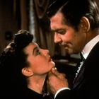 Eine Frau und ein Mann in eleganter Kleidung schauen sich intensiv an. Der Mann hebt das Kinn der Frau.