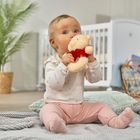 Ein Baby sitzt mit Kuscheltier auf einer Decke im Raum, umgeben von Pflanzen und Korbmöbel.