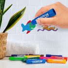 "Baff Paints" auf Stiften. Hand malt bunten Fisch. Geflochtener Pflanzenkorb, weiße Kachelwand, Handtuch daneben.