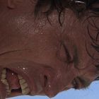 Eine Person mit angestrengtem Gesichtsausdruck, verschwitztem Gesicht und zusammengebissenen Zähnen vor klarem Himmel.