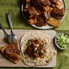 Zwei Maistortillas mit Rinderrippen und Frühlingszwiebeln, daneben Rippchen und eine Schale mit geschnittenen Lauchzwiebeln.