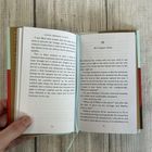Ein geöffnetes Buch zeigt Text im englischen Stil. Links Seite 22, rechts Seite 23 mit Kapitelüberschrift "We Compare Notes". Eine Hand hält die linke Seite. Der Hintergrund besteht aus Holzplanken.