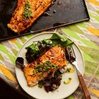 Kein Text. Ein gebratenes Lachsfilet liegt auf einem Teller mit frischen grünen Salatblättern und einer Gabel.