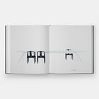 Die Seite zeigt zwei schwarze Stühle links und einen rechts an einem langen, weißen Tisch.